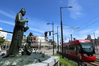 高岡駅前から出る万葉線の車両と大伴家持の銅像